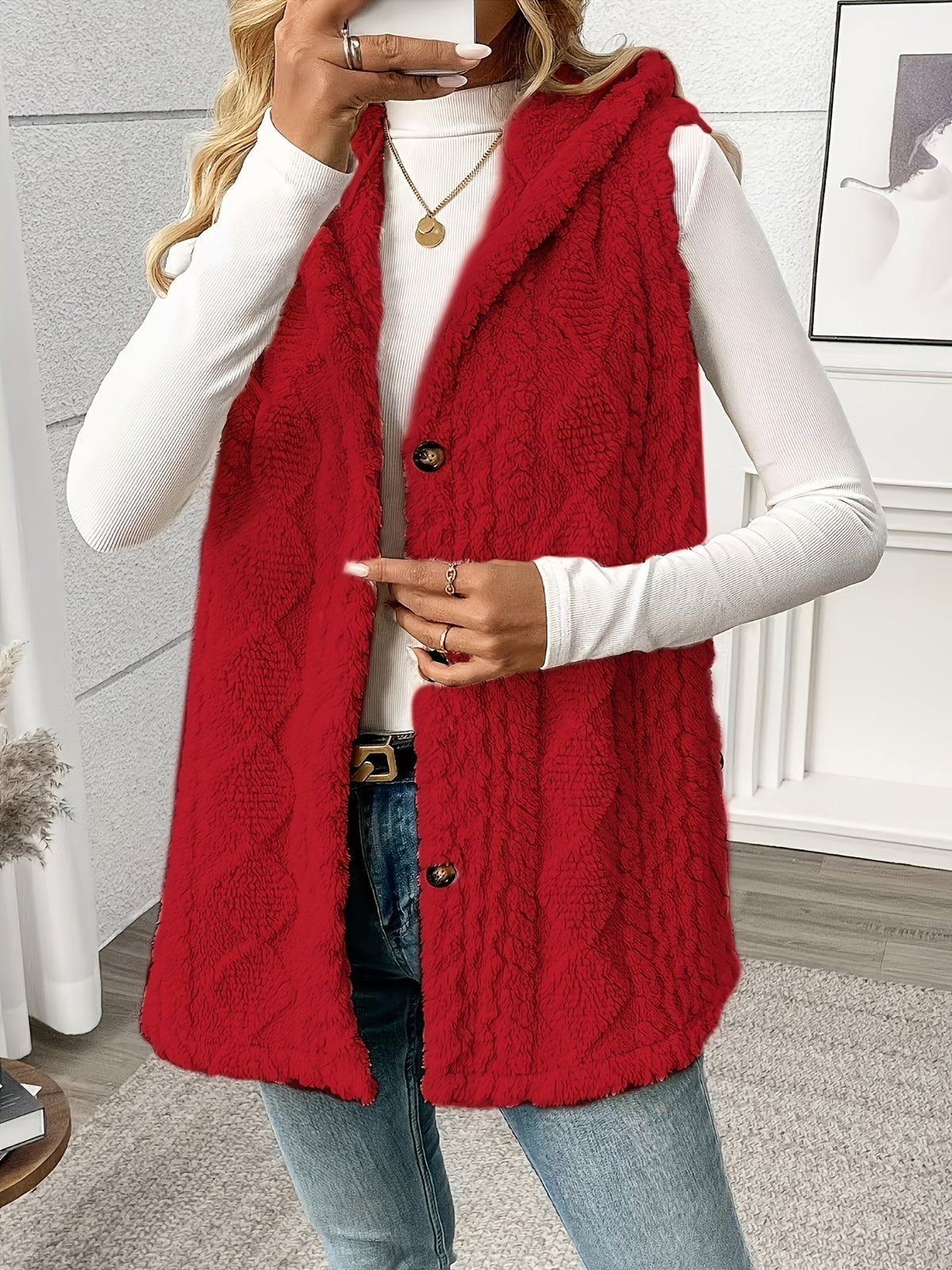 Person wearing a red knitted vest over a white long-sleeve shirt, standing indoors.