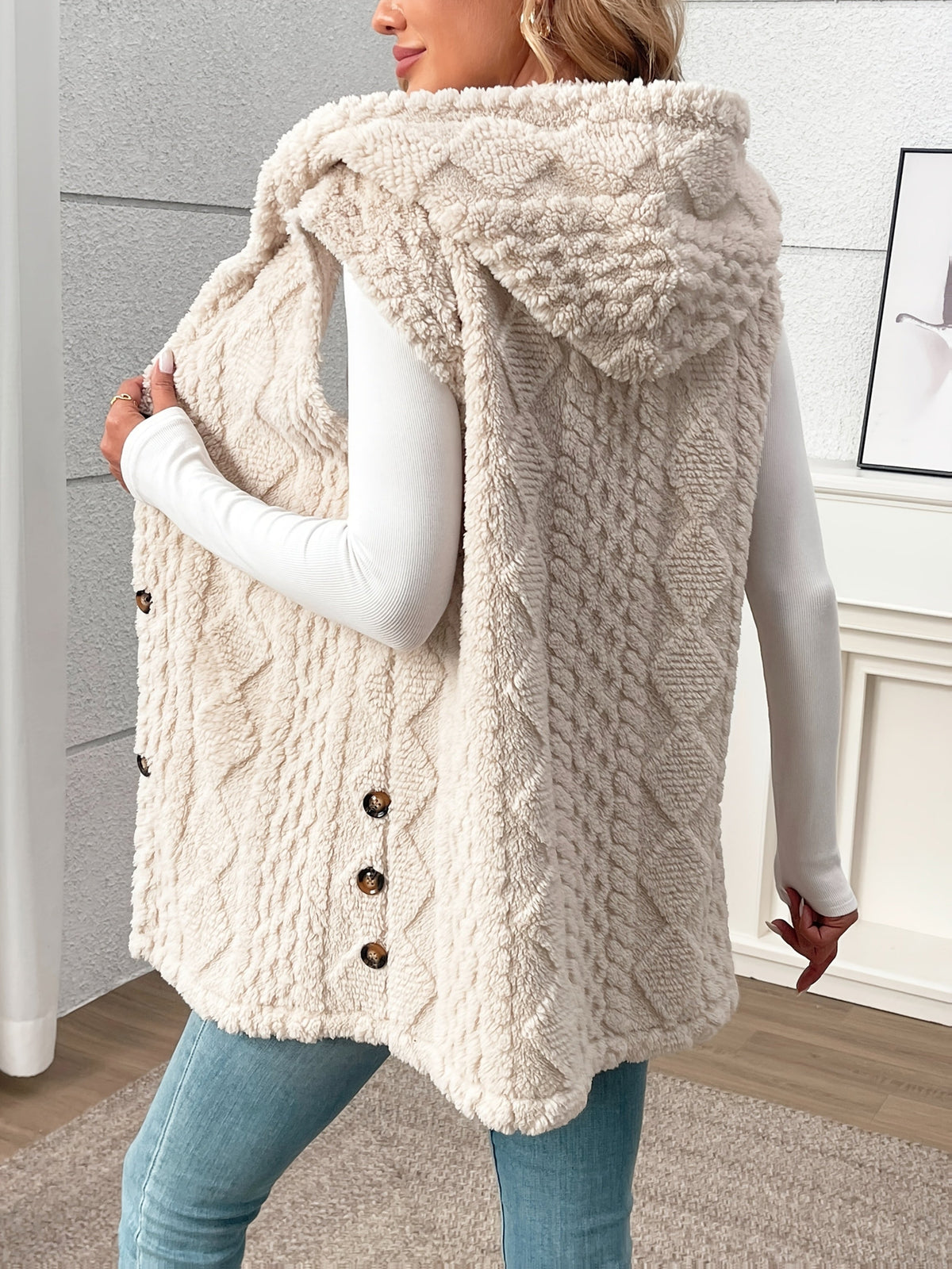 Person wearing a beige knitted vest with buttons indoors.