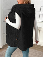 Person wearing a black quilted vest with buttons, standing indoors.