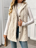 Person wearing a beige sherpa vest over a white long-sleeve shirt and jeans, holding a wooden object.
