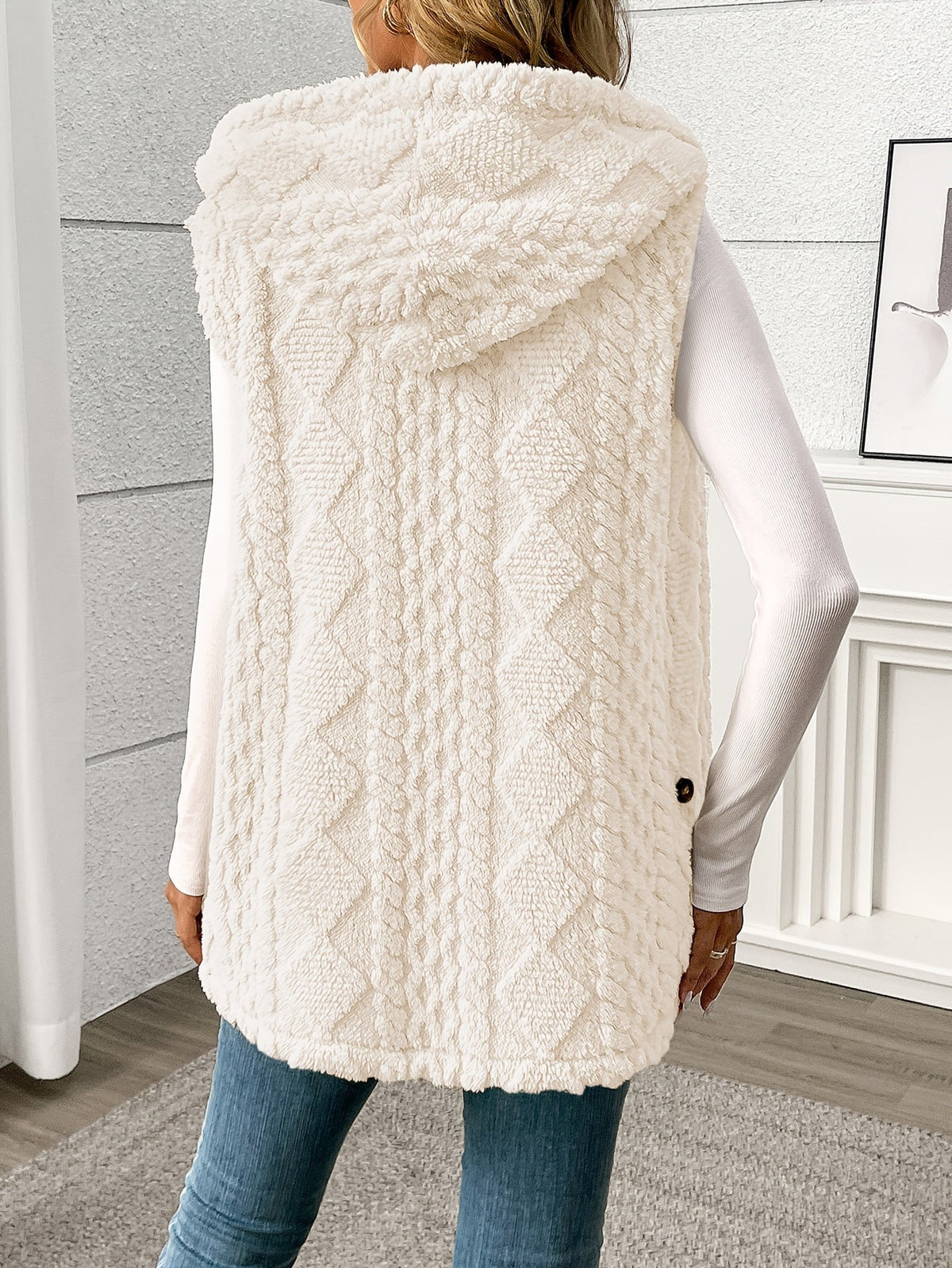 Person wearing a white cable knit vest in a room with a neutral background