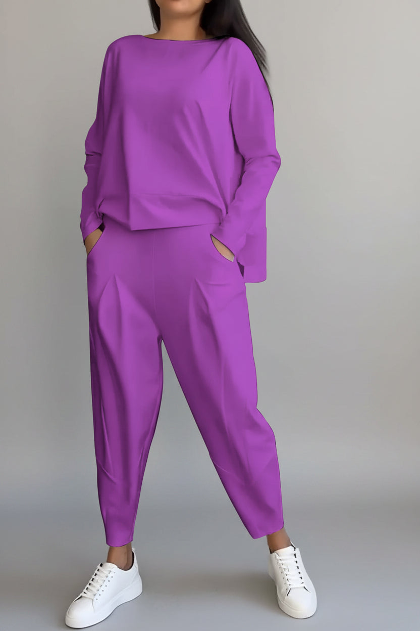 Person wearing a purple outfit with white sneakers against a gray concrete wall.