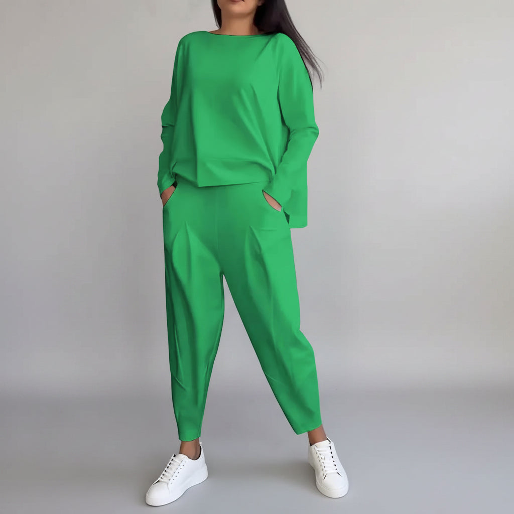 Person wearing a green outfit with white sneakers against a gray concrete wall.