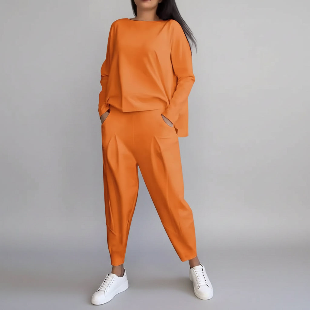 Person wearing an orange outfit with white sneakers against a gray concrete wall.