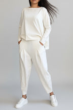 Person wearing a white outfit with high-waisted pants against a gray concrete wall.