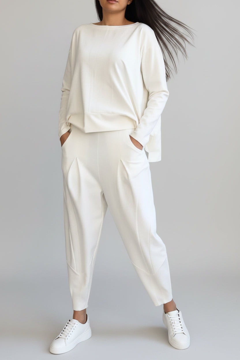 Person wearing a white outfit with high-waisted pants against a gray concrete wall.