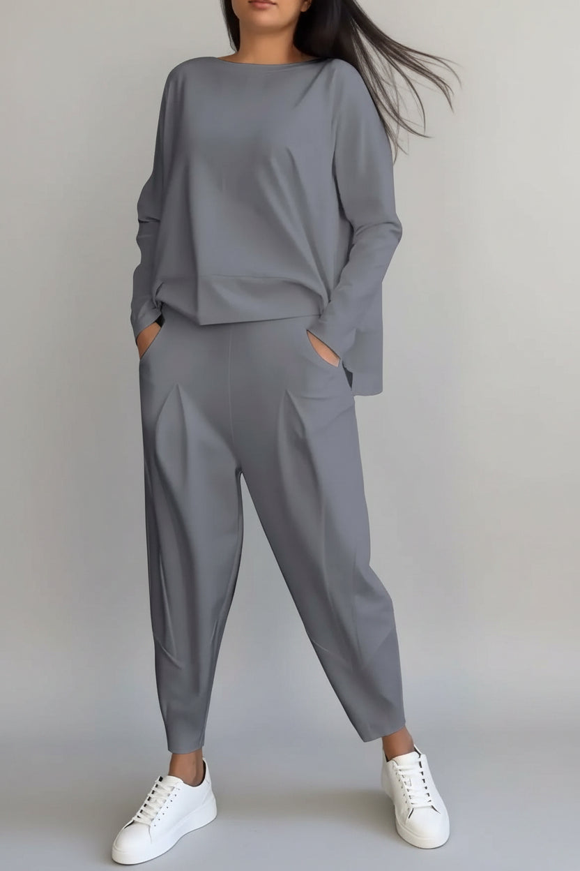 Person wearing a gray outfit with white sneakers against a concrete wall.