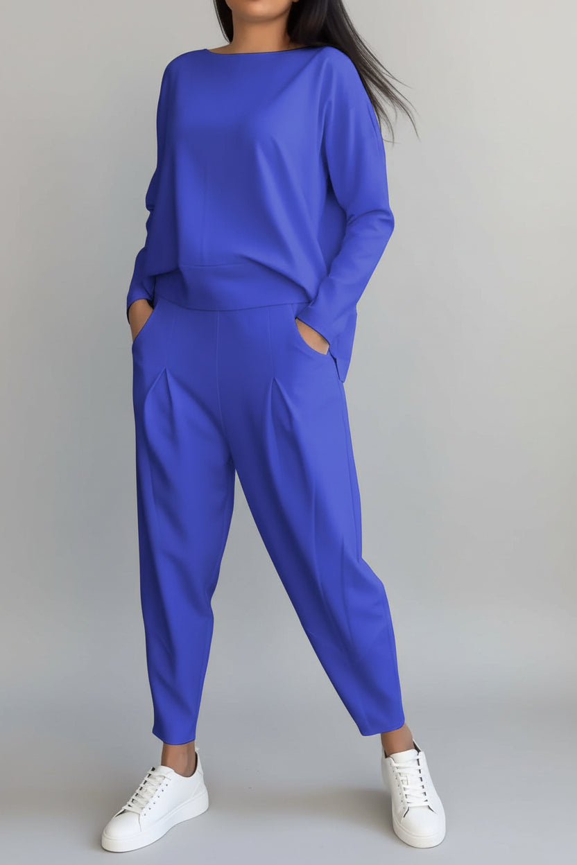 Person wearing a blue outfit with white sneakers against a gray concrete wall.