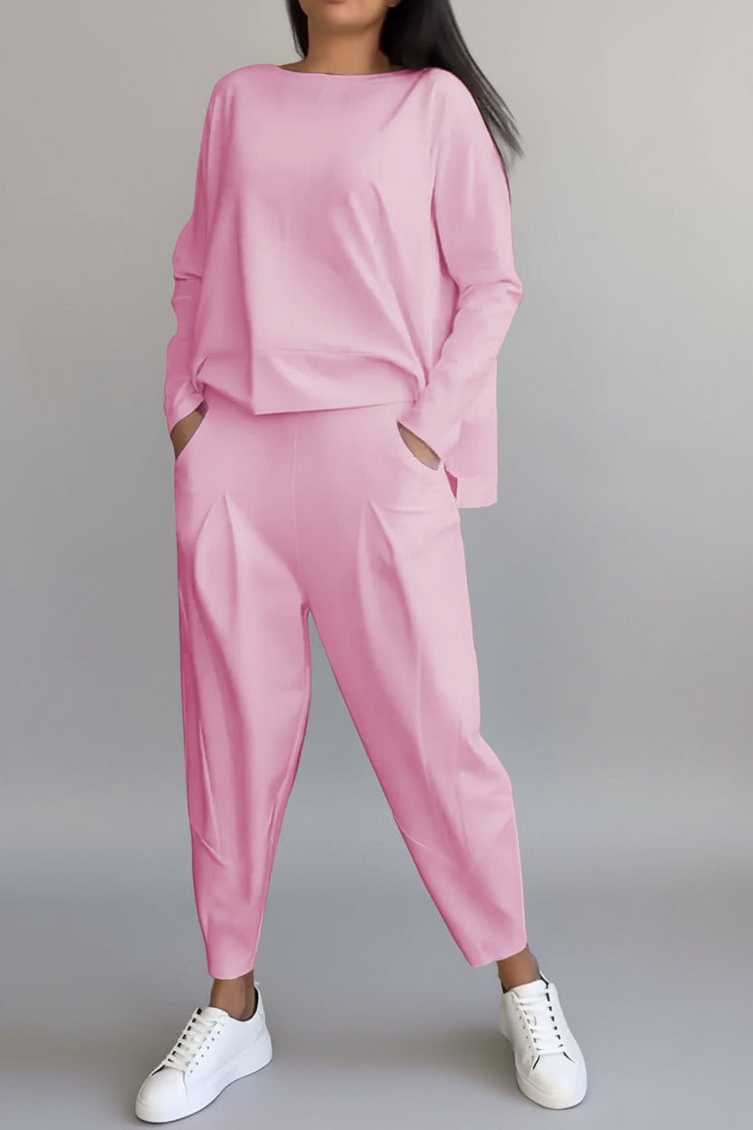 Person wearing a pink tracksuit with white sneakers against a gray concrete wall.