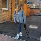 Woman in gray sweater and leggings standing on a sidewalk next to a brick building.