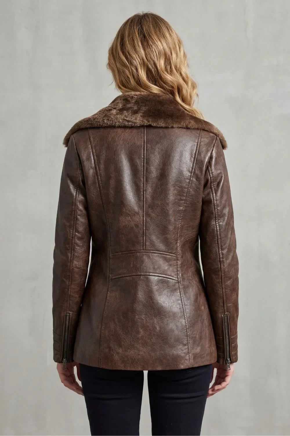 Brown leather jacket with fur collar worn by a person on a gray background
