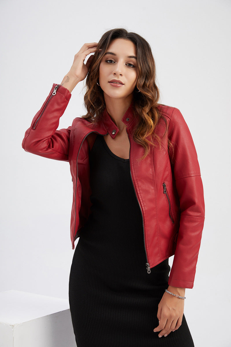 A woman wearing a cropped red faux-leather moto jacket over a black ribbed dress, posing against a light gray studio background.