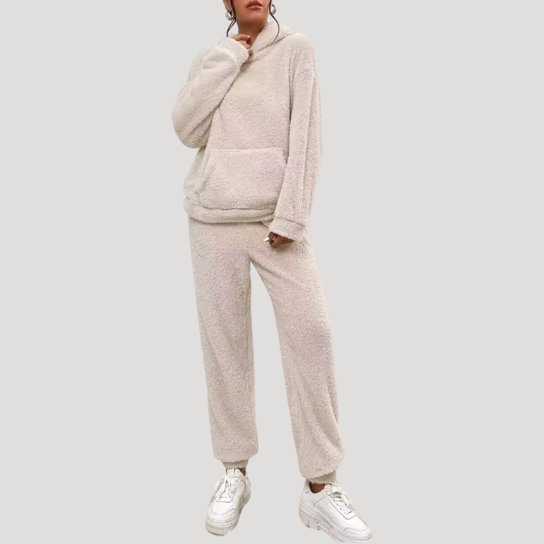 Person wearing a beige fleece tracksuit with white sneakers on a light gray background