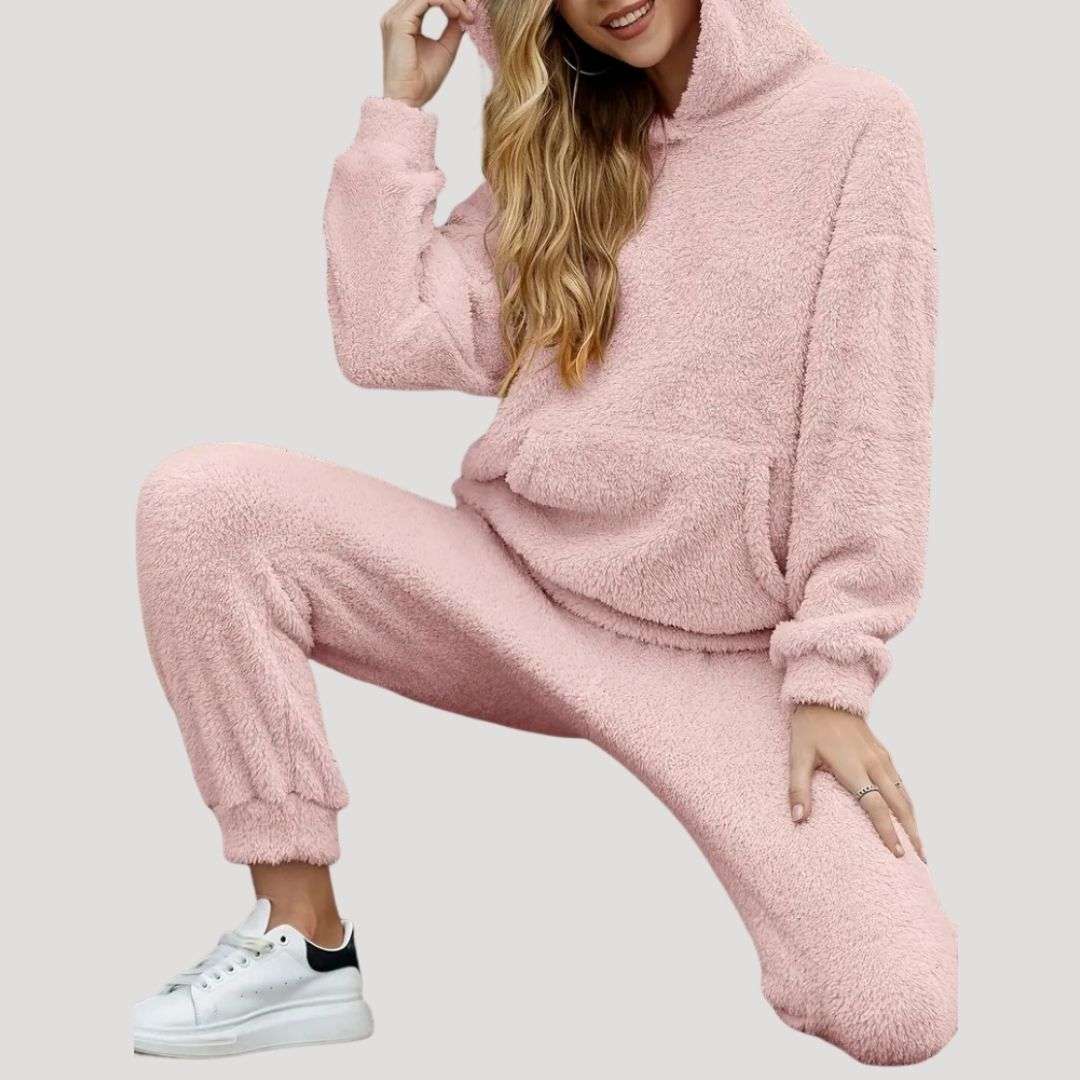 Person wearing a pink fleece tracksuit with white sneakers on a light gray background