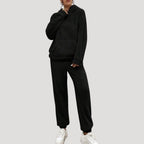 Person wearing a black tracksuit with white sneakers on a light gray background