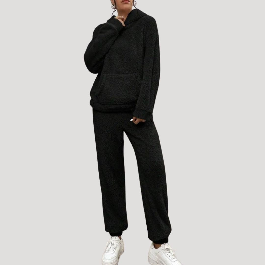 Person wearing a black tracksuit with white sneakers on a light gray background