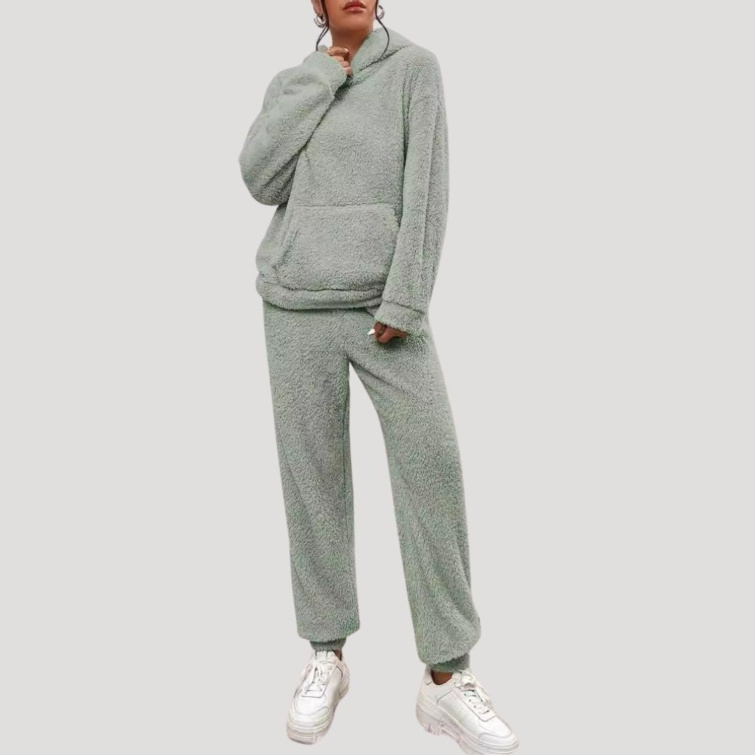 Person wearing a gray fleece tracksuit with white sneakers on a light gray background