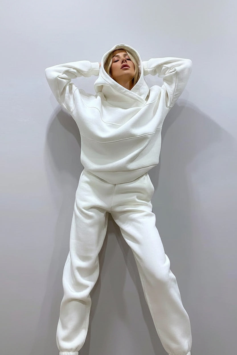 A person wearing a matching white lounge set consisting of a high-neck pullover hoodie and wide-leg sweatpants, posed against a plain light gray wall.