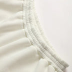 Close-up of a white or off-white pleated fabric garment detail with gathered elastic seams on a plain light background.