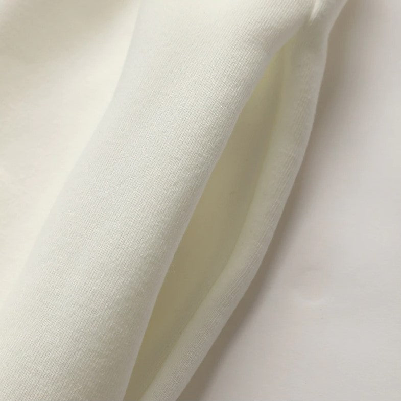 A close-up of soft off-white fabric draped in folds, showing a smooth knit texture and a slightly sheer inner layer.