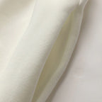 A close-up of soft off-white fabric draped in folds, showing a smooth knit texture and a slightly sheer inner layer.