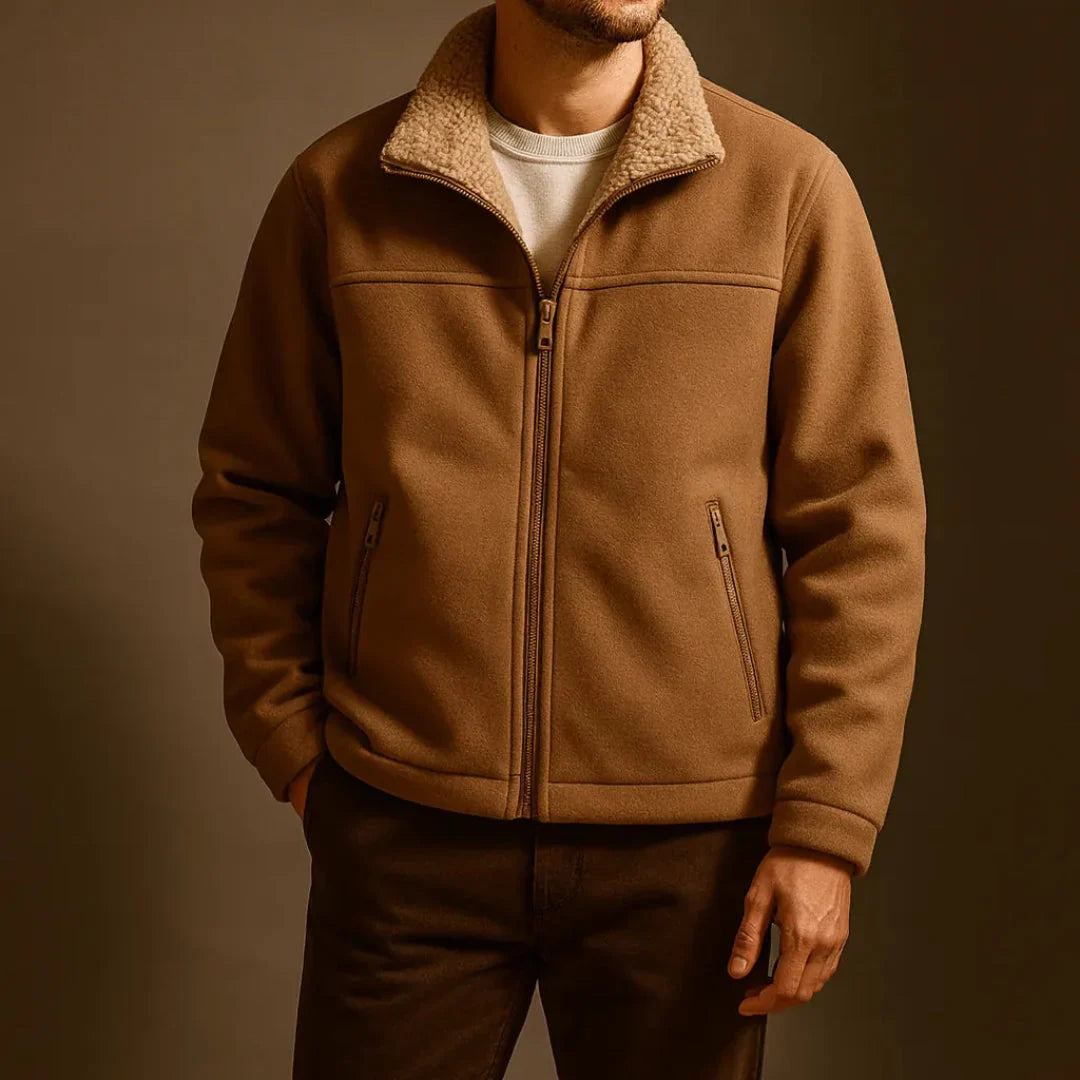 A man wearing a brown sherpa-lined zip-up fleece jacket over a white t-shirt and dark brown pants, photographed against a dark brown studio background.