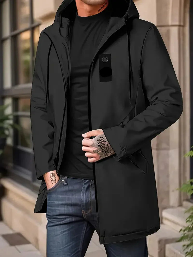 Person wearing a black jacket with a hood, black shirt, and blue jeans in an urban setting.