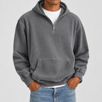 A man wearing a gray quarter-zip pullover hoodie with a front kangaroo pocket, layered over a white t-shirt and blue jeans, shown from the neck down against a plain white background.