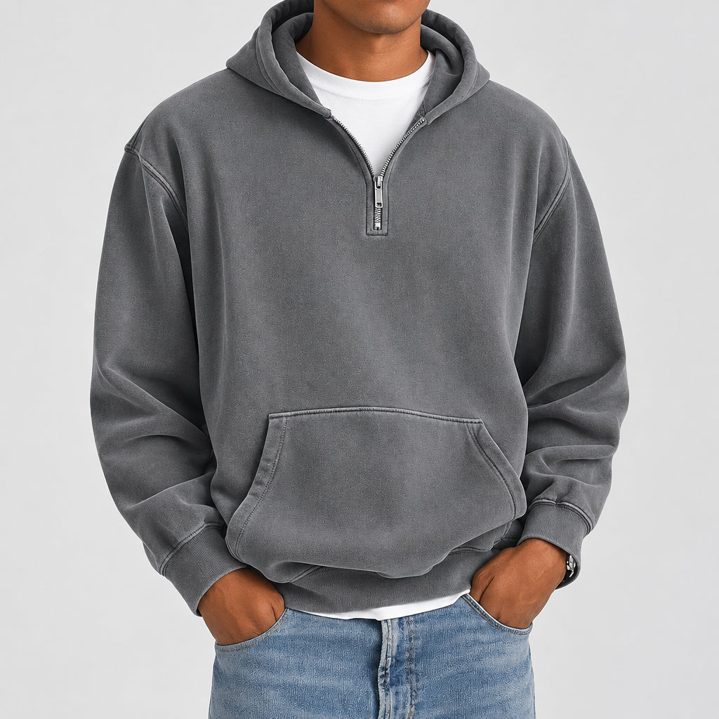 A man wearing a gray quarter-zip pullover hoodie with a front kangaroo pocket, layered over a white t-shirt and blue jeans, shown from the neck down against a plain white background.