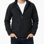 A man wearing a black hooded zip-up jacket over a white t-shirt and dark blue jeans, shown from the neck down against a plain white background.