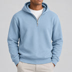 A close-up of a person wearing a light blue half-zip hoodie over a white t-shirt, cropped from the chin down against a plain white background.