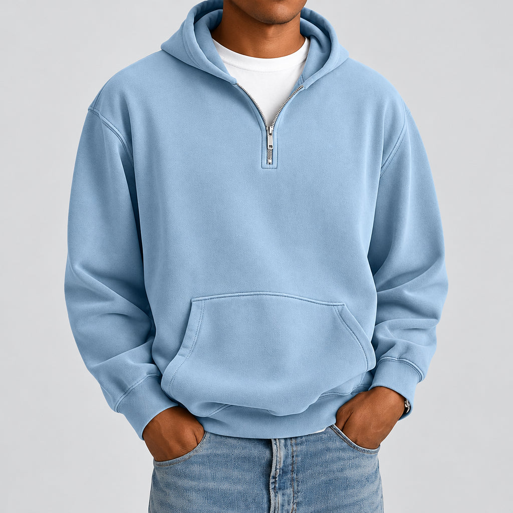 A man wearing a light blue half-zip hoodie with a kangaroo pocket, layered over a white t-shirt and blue jeans, shown from the neck down against a plain white background.